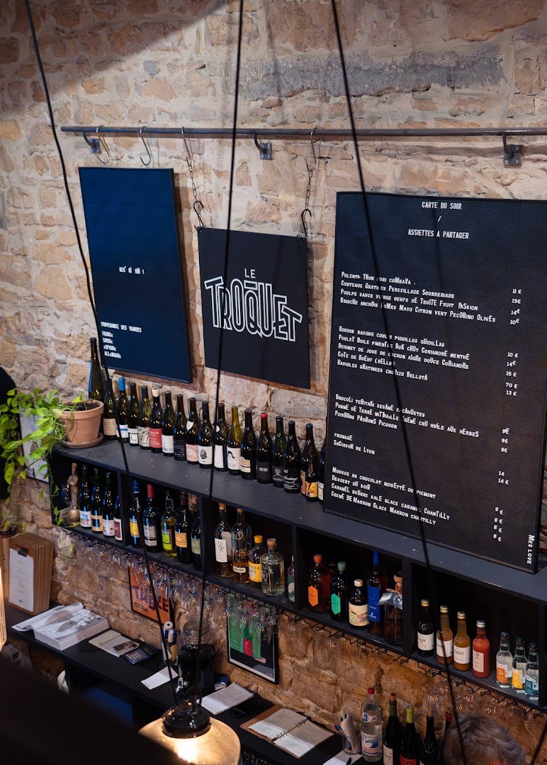 Le mur de pierre du Troquet avec ses bouteilles et ses ardoises